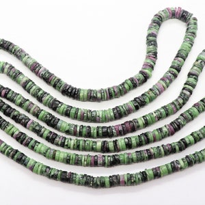May include: Strands of gemstone beads. The beads are flat, disc-shaped, and feature a mix of green, black, and reddish-purple colors. The beads are strung together, creating a necklace or bracelet material. The background is plain white.