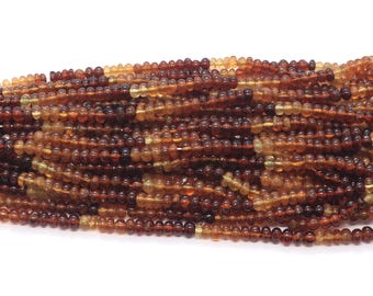 May include: A bundle of small, round beads in shades of brown and amber. The beads are strung together, creating a textured, layered appearance. The beads are on a white background.