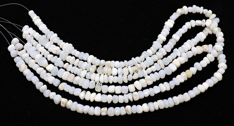 May include: A strand of white gemstone beads, with a slightly irregular, pebble-like shape. The beads are strung on a thin wire and are arranged in a loose, flowing pattern.