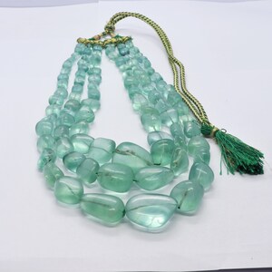 Può includere: Una collana multifilo realizzata con perline di forma arrotondata, sfaccettate, di colore verde chiaro. La collana ha un fiocco verde all'estremità del cordoncino.