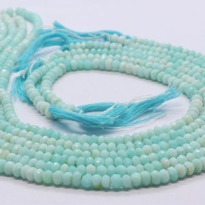 May include: A strand of light blue gemstone beads, likely aquamarine or opal, with a faceted finish. The beads are strung on a thin thread and are arranged in a circular pattern. The beads are approximately 4mm in diameter.