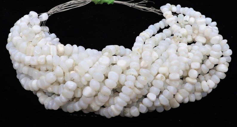 May include: A strand of white gemstone beads, each bead is a smooth, irregular oval shape. The beads are strung on a silver wire.