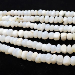 May include: A strand of white gemstone beads, with a smooth, rounded shape. The beads are strung together on a clear thread, and the strand is laid out in a loose coil.