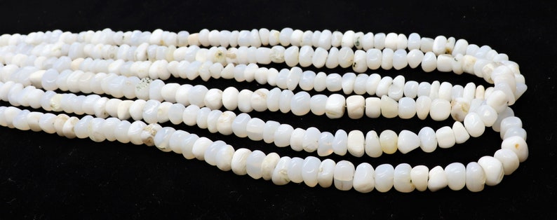 May include: A strand of white gemstone beads, with a smooth, rounded shape. The beads are strung together on a clear thread, and the strand is laid out in a loose coil.