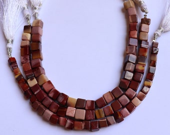 May include: A strand of red, brown, and cream colored gemstone beads. The beads are square shaped and have a polished finish. The beads are strung on a cord and have tassels on the ends.