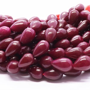 May include: A cluster of deep burgundy, teardrop-shaped beads. The beads are strung together, creating a dense, textured appearance. The beads have a glossy finish, reflecting light. The overall theme suggests jewellery making or crafting supplies.