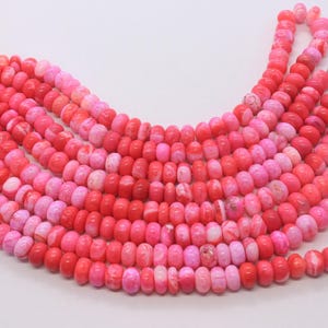 May include: Strands of pink and red beads in varying shades, creating a gradient effect. The beads are small, round, and strung together, perfect for jewelry making. The color palette ranges from light pink to deep red.