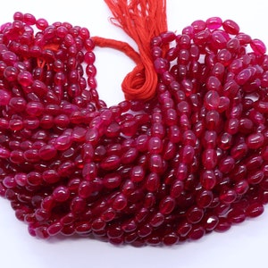 Può includere: Una collana di perle ovali di pietra preziosa di colore rosso scuro. Le perle sono lisce e lucidate e sono infilate su un filo rosso.