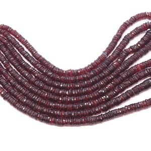 Può includere: Più fili di perline di pietre preziose rosso scuro, probabilmente granato, su sfondo bianco. Le perline, piccole e piatte, hanno una forma a disco con una superficie sfaccettata. Sono infilate, formando più fili.