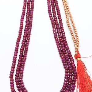 May include: A three-strand necklace made of faceted ruby beads. The necklace has a gold tassel at the end.