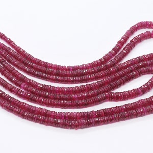 Può includere: Una collana di perle di rubino rosso scuro, ogni perla è sfaccettata e ha una forma leggermente arrotondata. Le perle sono infilate su un filo sottile e sono disposte in un motivo sciolto e fluido.