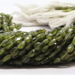 以下が含まれることがあります： 緑色のペリドットビーズのストランド。各ビーズはファセットカットされており、涙の形状をしています。ビーズは白い糸に糸通しされています。