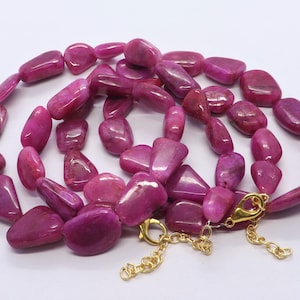 May include: A pink gemstone necklace with a gold clasp. The necklace is made of multiple strands of smooth, flat, oval-shaped stones.