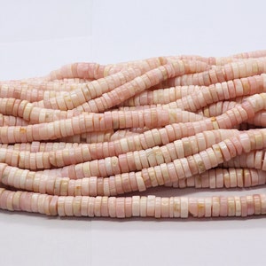 Pode incluir: Um fio de contas planas e redondas rosa e brancas. As contas s&atilde;o empilhadas, criando um conjunto espesso e texturizado. As contas s&atilde;o uma mistura de rosa p&aacute;lido e branco, com um leve brilho iridescente. As contas s&atilde;o enfiadas em um cord&atilde;o branco.