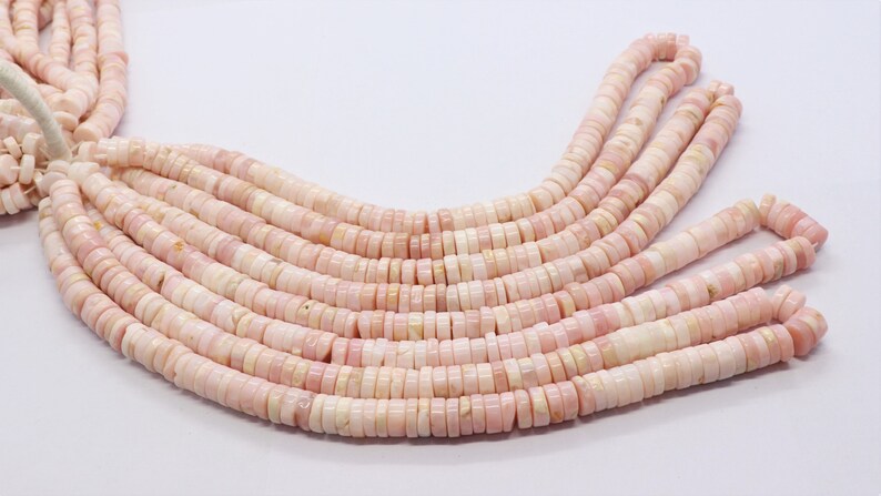 Pode incluir: Fios de contas de concha rosa e branca. As contas s&atilde;o planas, em forma de disco e enfiadas. A cor &eacute; rosa pastel suave com detalhes brancos. As contas est&atilde;o dispostas em um padr&atilde;o em cascata.