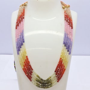 Può includere: Collana multifilo con perline di pietre preziose sfaccettate in tonalità di viola, rosa, arancio, rosso, giallo e verde. La collana è composta da più fili di perline, ogni filo di un colore diverso.