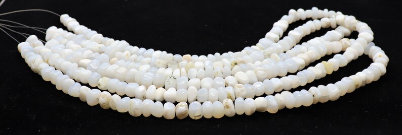 May include: A strand of white gemstone beads, likely moonstone, with a slightly irregular, rounded shape. The beads are strung on a thin wire and are arranged in a loose, flowing pattern.