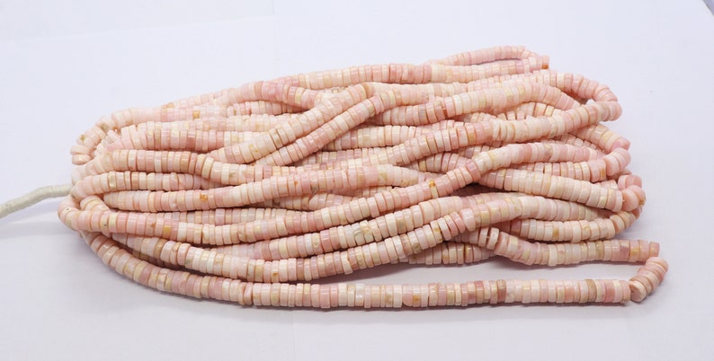 Pode incluir: Um conjunto de contas planas e redondas rosa e creme, enfiadas juntas. As contas s&atilde;o uniformes em tamanho e forma, com uma superf&iacute;cie ligeiramente irregular. As contas s&atilde;o provavelmente feitas de um material natural, como pedra ou concha.