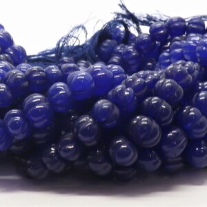 May include: A strand of blue glass beads with a faceted, flower-like design. The beads are strung on a thin cord.