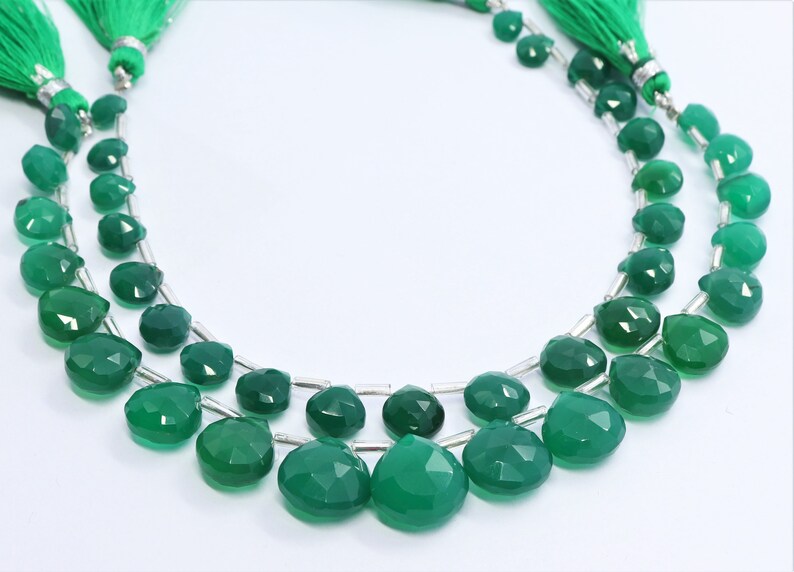 Puede incluir: Una hebra de cuentas de piedras preciosas verdes, con forma de l&aacute;grima facetada. Las cuentas est&aacute;n enhebradas en alambre plateado y tienen un borla en cada extremo.