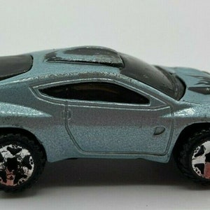 May include: A light blue toy car with black accents and a black roof. The car has a detailed interior and large wheels.