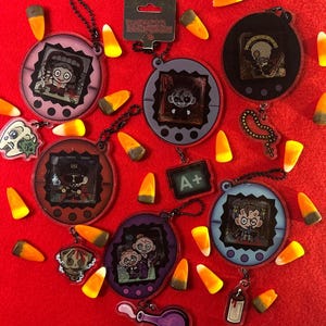 May include: A collection of circular acrylic keychains featuring cartoon character illustrations inside digital pet-style frames, accompanied by small dangling charms and scattered candy corn pieces. One keychain includes a tag labelled Death Note Despair.