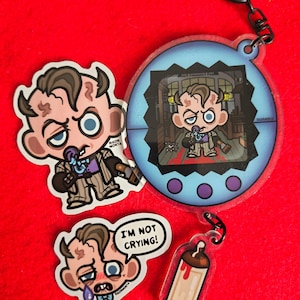 Può includere: Un set di due adesivi e un portachiavi circolare in acrilico con un personaggio dei cartoni animati con capelli castani, abito gessato e papillon blu. Un adesivo include il testo I'M NOT CRYING! e un ciondolo a biberon pende dal portachiavi.