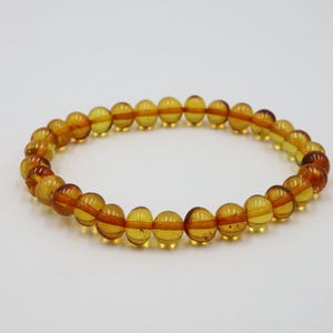 May include: A bracelet made of amber beads. The beads are a warm, honey color and are strung on a clear elastic cord.