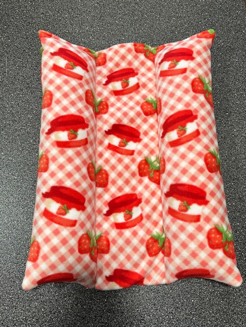 May include: A red and white gingham fabric heating pad with a strawberry pattern. The pad is divided into three sections.