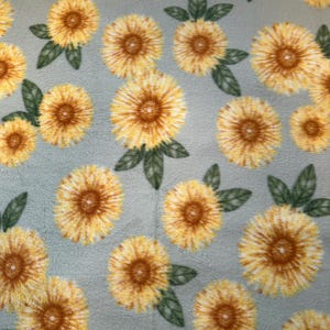 May include: A light blue fabric with a repeating pattern of yellow sunflowers with green leaves.