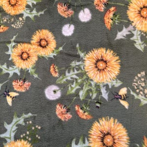 May include: A green fabric with a repeating pattern of yellow dandelions and bees. The fabric has a soft, fuzzy texture.