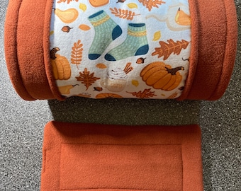 Könnte beinhalten: Ein brauner, mit Fleece gefütterter Tunnel mit einer weißen Stoffauskleidung, die mit einem Herbstmotiv bedruckt ist, das Kürbisse, Blätter und Socken zeigt. Der Tunnel wird mit einem passenden flachen Bett aus braunem Fleece geliefert.