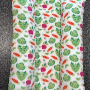 May include: Two white rectangular cushions with a repeating pattern of green leafy vegetables, orange carrots, and pink radishes. The cushions are sewn together to create a larger cushion.