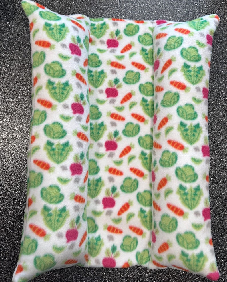 May include: Two white rectangular cushions with a repeating pattern of green leafy vegetables, orange carrots, and pink radishes. The cushions are sewn together to create a larger cushion.