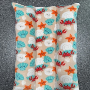 May include: A beige pillow with a repeating pattern of seashells, starfish, and crabs. The pillow is divided into three sections.