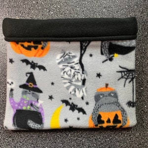 May include: A gray fleece cat bed with a black fleece trim. The bed has a Halloween theme with images of cats, pumpkins, bats, and ghosts.