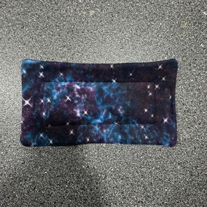 May include: A dark blue and purple fleece pet bed with a galaxy print. The bed has a white border and white stars throughout the print.
