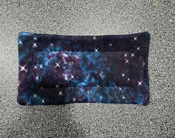 May include: A dark blue and purple fleece pet bed with a galaxy print. The bed has a white border and white stars throughout the print.