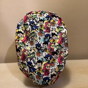 Puede incluir: Un gorro de quirófano colorido con un patrón repetido de personajes de dibujos animados del programa de televisión Teen Titans Go! Los personajes están en varias poses y expresiones, y el gorro es de color amarillo brillante con un fondo blanco.
