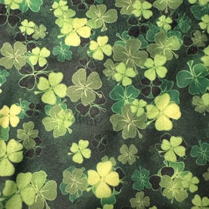 May include: Green fabric with a repeating pattern of four-leaf clovers. The clovers are in shades of green and yellow.