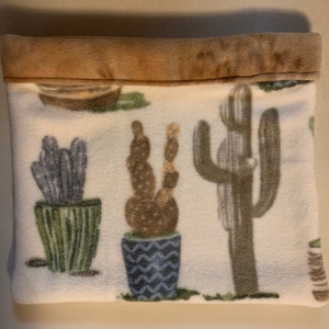 May include: A white fleece pillow with a brown suede trim. The pillow has a cactus print with different colored cacti in pots.