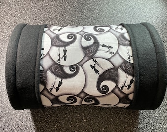 Könnte beinhalten: Ein schwarzes und weißes zylindrisches Haustierbett mit einem Nightmare Before Christmas-Druck. Das Bett ist aus weichem Stoff und hat einen schwarzen Fleece-Besatz.