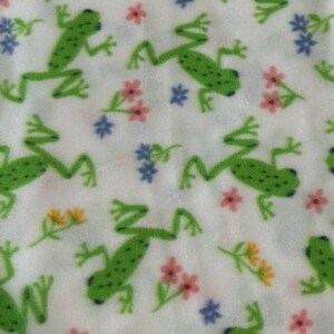 May include: White fabric with a repeating pattern of green frogs and colorful flowers. The frogs are in various poses, some are jumping, some are sitting, and some are looking up.