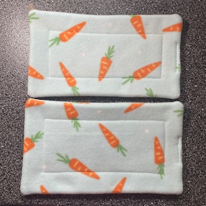 May include: Two light blue fleece pet beds with a carrot pattern. The beds have a white border and a white stitched seam around the edge.