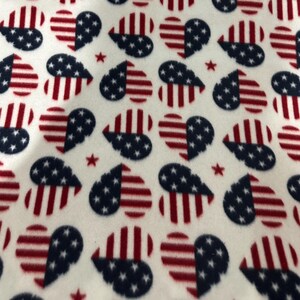 May include: A white fabric featuring a repeating pattern of hearts. Each heart is divided vertically, with one half displaying red and white horizontal stripes and the other half featuring a dark blue background with small white stars. Small red stars are scattered between the hearts.