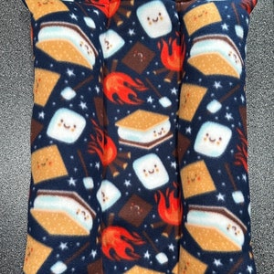 May include: A blue fleece cushion with a pattern of s'mores, flames, and stars. The cushion is divided into three sections.