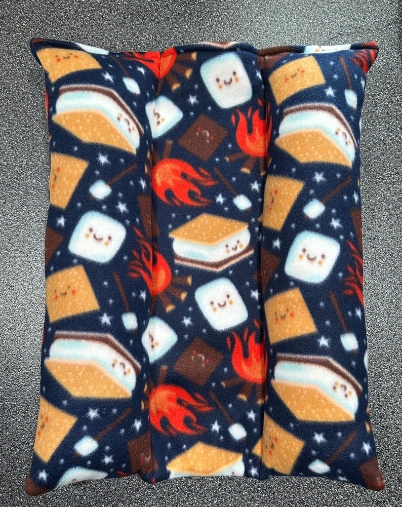 May include: A blue fleece cushion with a pattern of s'mores, flames, and stars. The cushion is divided into three sections.