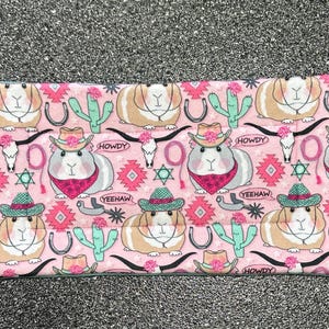 May include: Pink fabric with a repeating pattern of guinea pigs wearing cowboy hats and holding lassos. The fabric also features cacti, horseshoes, and the words "Howdy" and "Yeehaw".