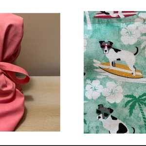May include: A pink scrub cap with a bow fastening. The fabric is a solid, light coral colour. The second image shows a teal fabric with a pattern of dogs surfing on yellow surfboards, palm trees, and white flowers.