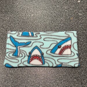 May include: A blue and white fleece fabric with a shark pattern. The sharks are swimming in a blue ocean with white waves.